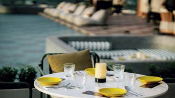 Une table à manger avec des assiettes jaunes, des verres transparents et une bougie, le tout disposé devant une vue sur la piscine.