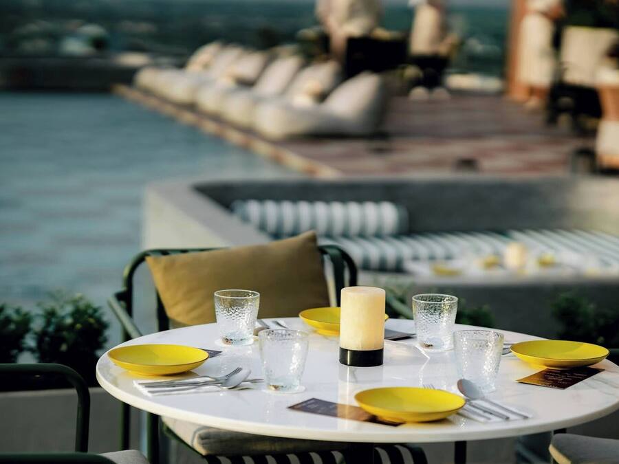 Une table à manger avec des assiettes jaunes, des verres transparents et une bougie, le tout disposé devant une vue sur la piscine.