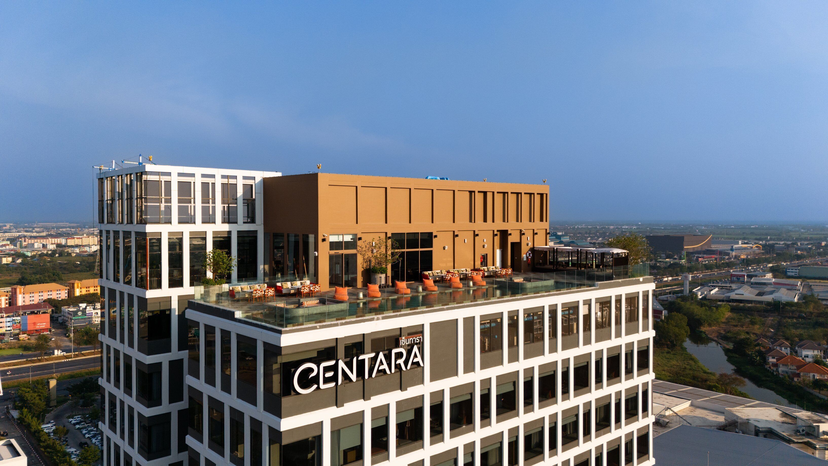 Un hotel de varios pisos con una terraza en la azotea que cuenta con asientos al aire libre y vistas de la ciudad.