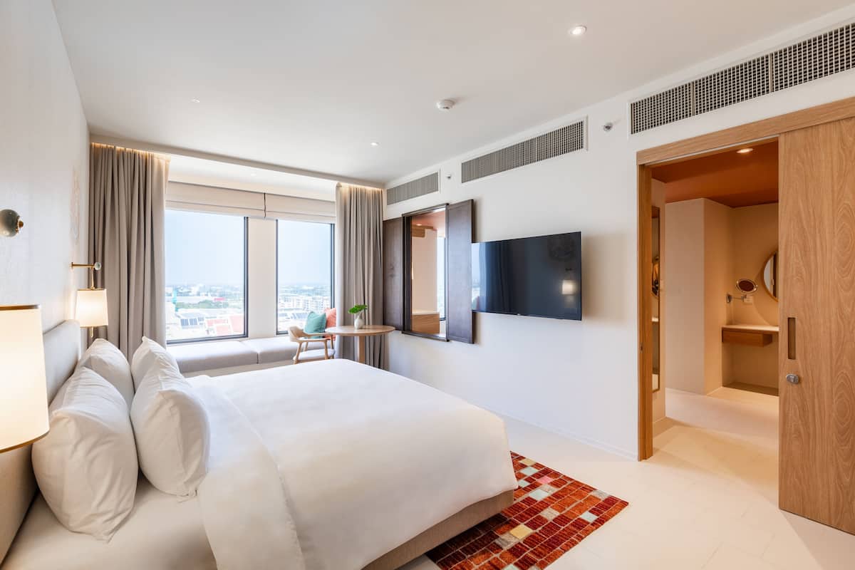 Een moderne hotelkamer met een groot bed, een aan de muur bevestigde televisie, een raam met gordijnen en uitzicht op de stad.