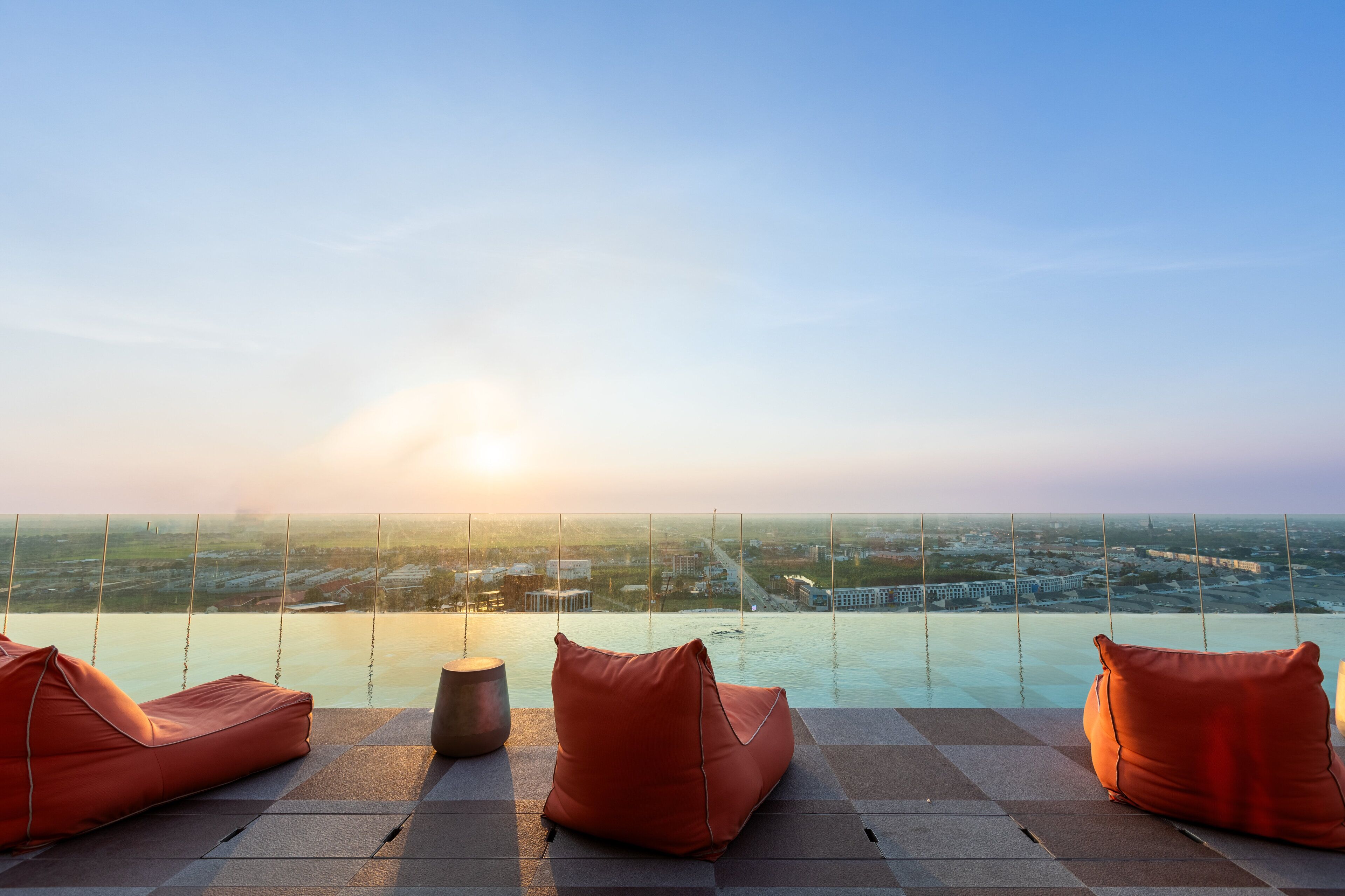 A rooftop terrace with a view of the city at sunset, featuring two orange bean bags and a round table.