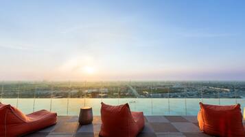 A rooftop terrace with a view of the city at sunset, featuring two orange bean bags and a round table.