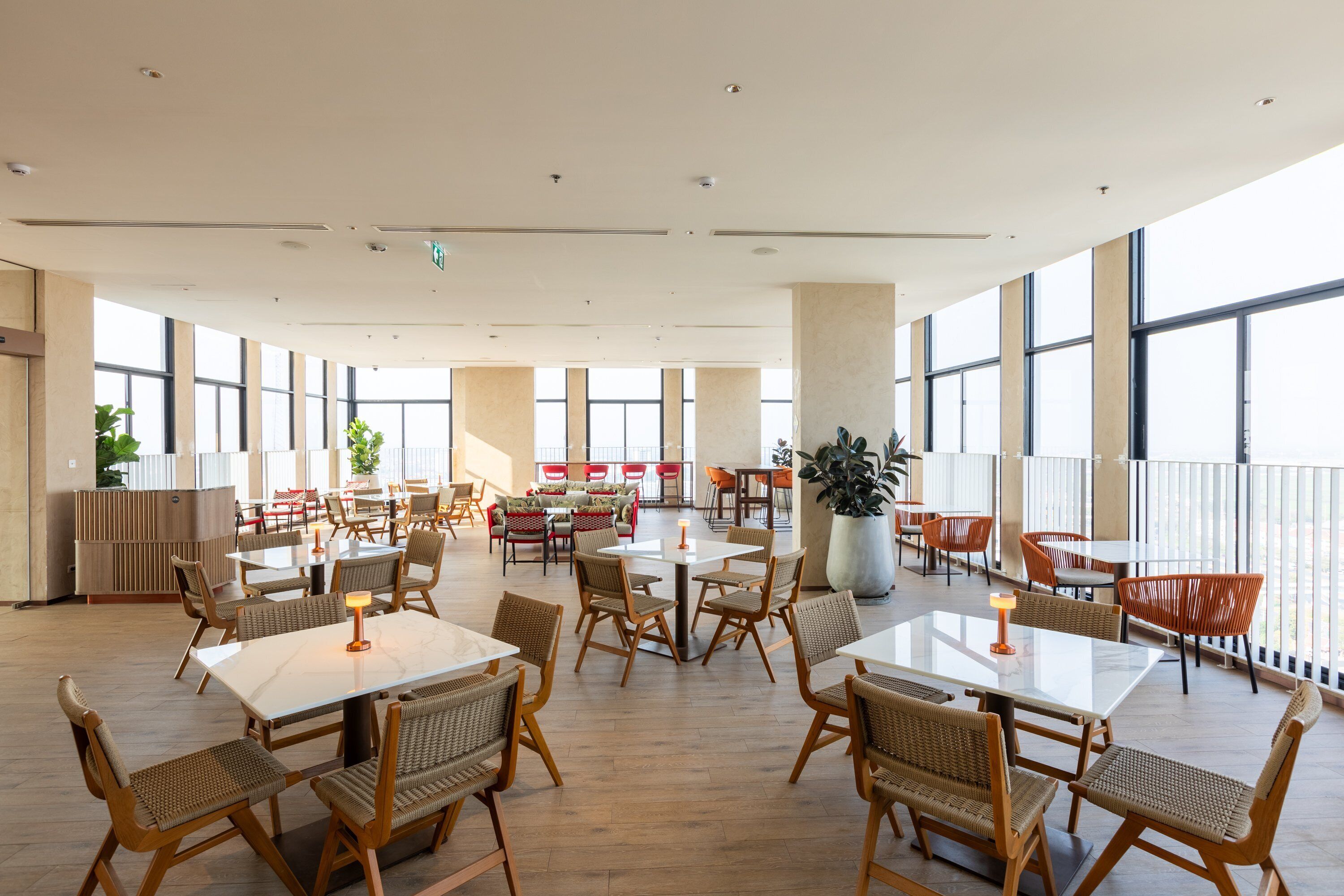 Un comedor interior amplio con techos altos, ventanas grandes y diversas opciones de asientos, incluyendo mesas y sillas.