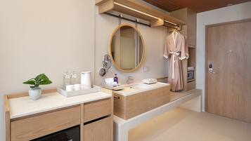 A modern bathroom with a wooden vanity, a large mirror, a robe hanging on the wall, and a built-in oven.