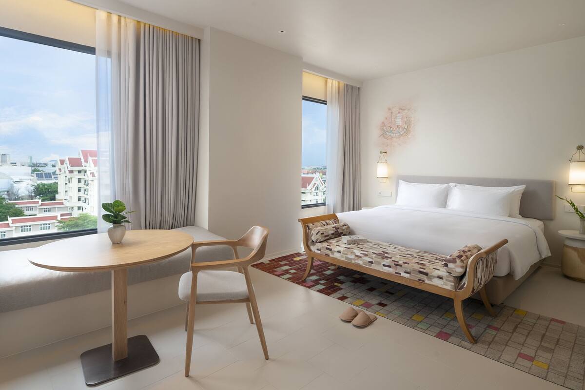 Hotelkamer met een bed, bureau, stoel, raam met gordijnen en uitzicht op gebouwen.