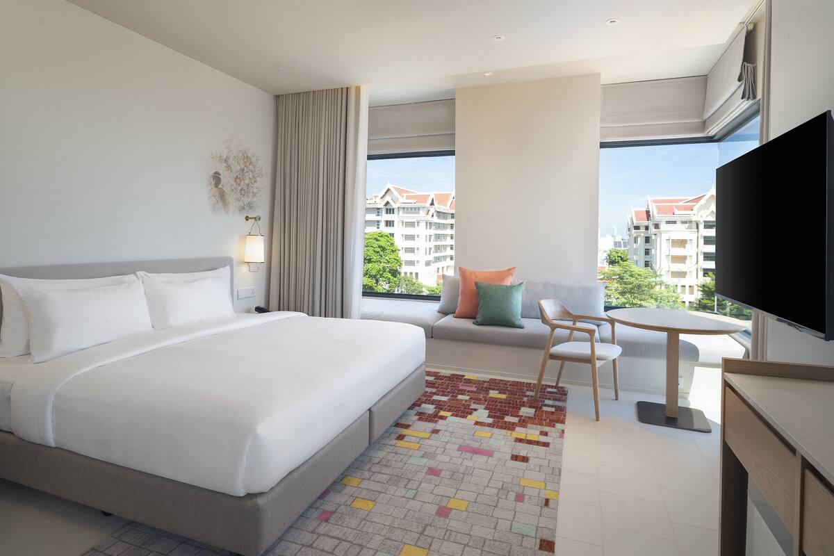 Een moderne hotelkamer met een groot bed, een kleine zithoek, een televisie en een balkon met uitzicht op de stad.
