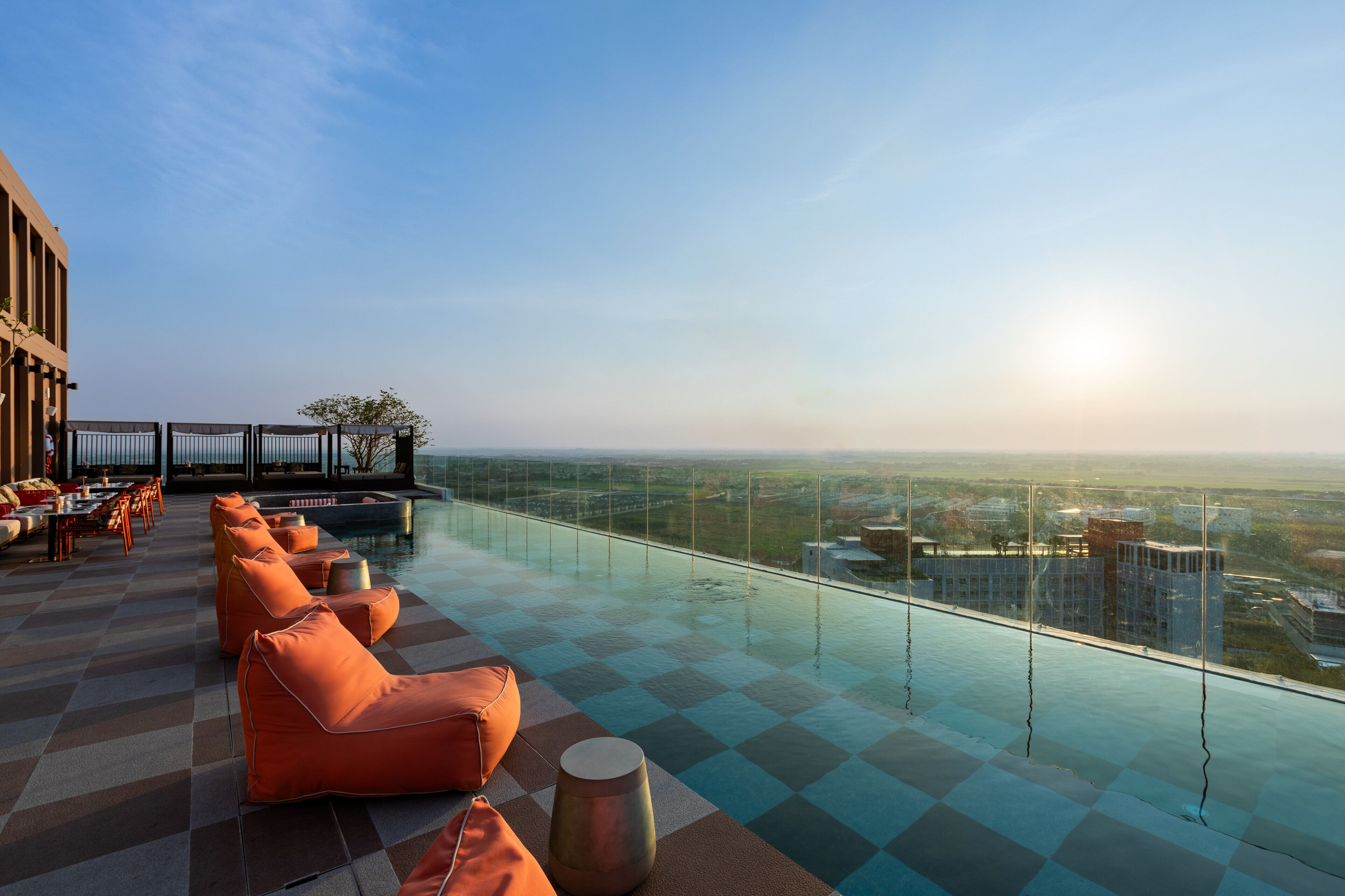 A rooftop infinity pool with orange seating and a city view.