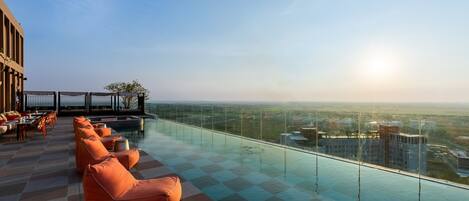 A rooftop infinity pool with orange seating and a city view.