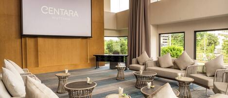 A spacious room with a large screen displaying "CENTARA AYUTTHAYA", wicker furniture, and a view of greenery outside.