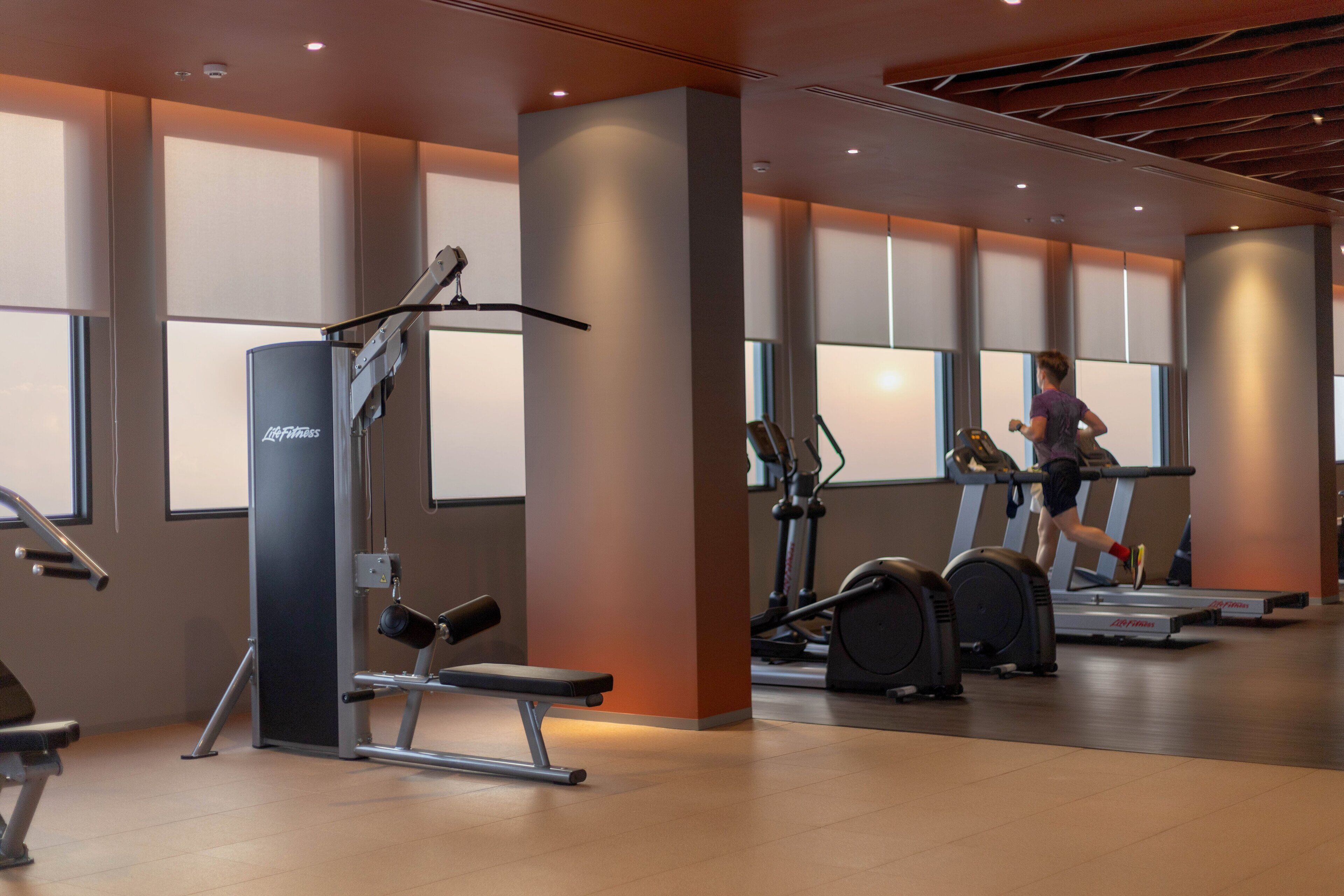 Une salle de sport équipée de matériel d’exercice, d’un tapis de course et où une personne est en train de courir.