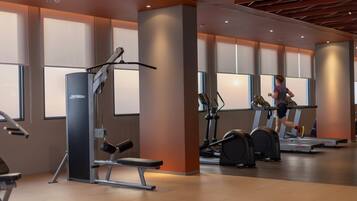 Une salle de sport équipée de matériel d’exercice, d’un tapis de course et où une personne est en train de courir.