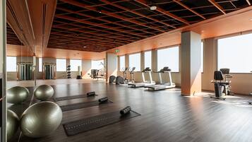 Een ruime fitnessruimte met trainingsapparatuur, grote ramen en een houten plafond.