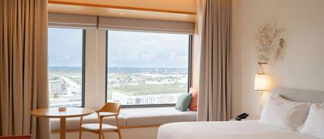 A hotel room with a bed, a window seat with a view, a small table, and a chair.