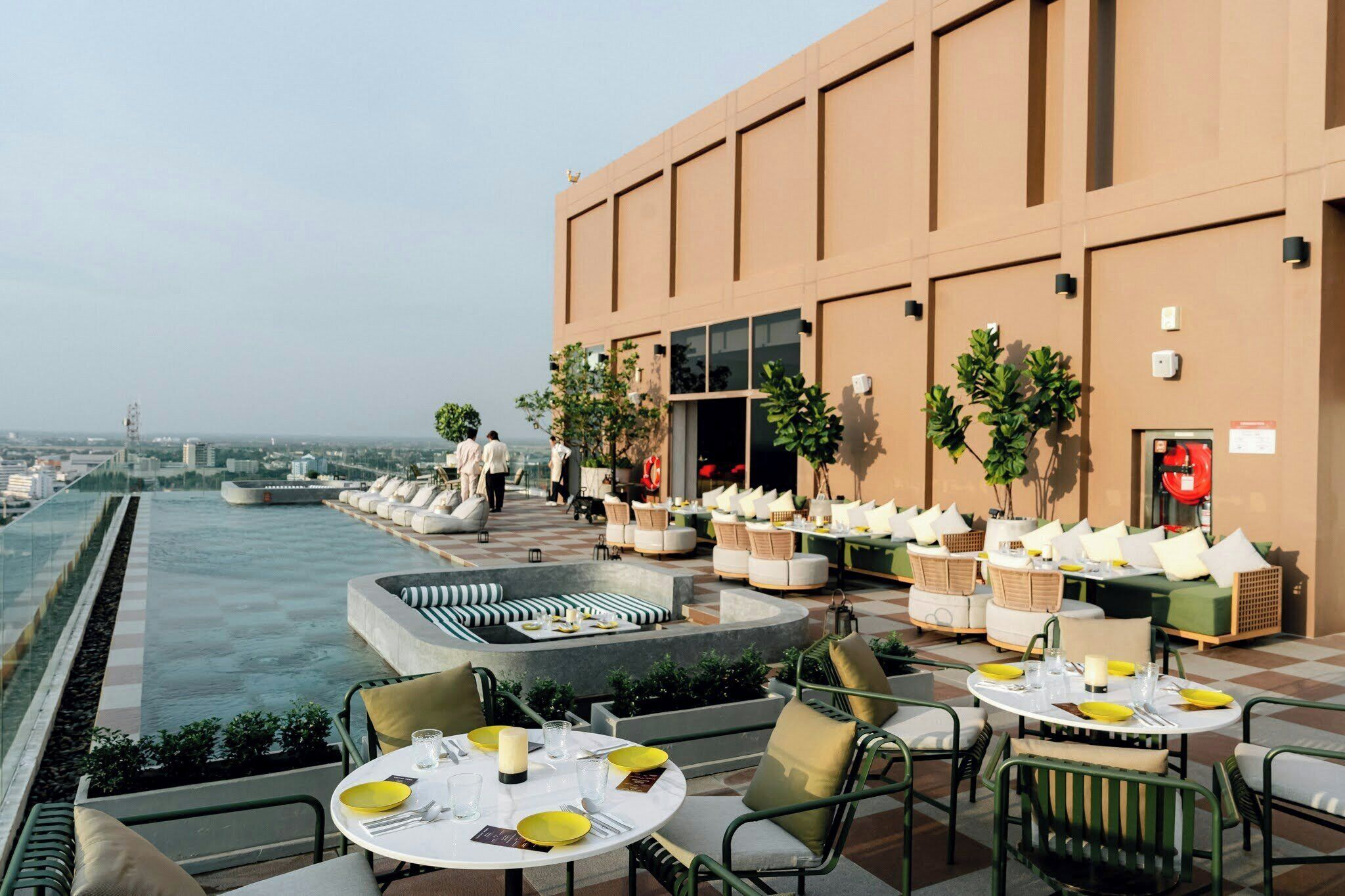 A rooftop terrace with outdoor seating, a pool, and a view of the city skyline.