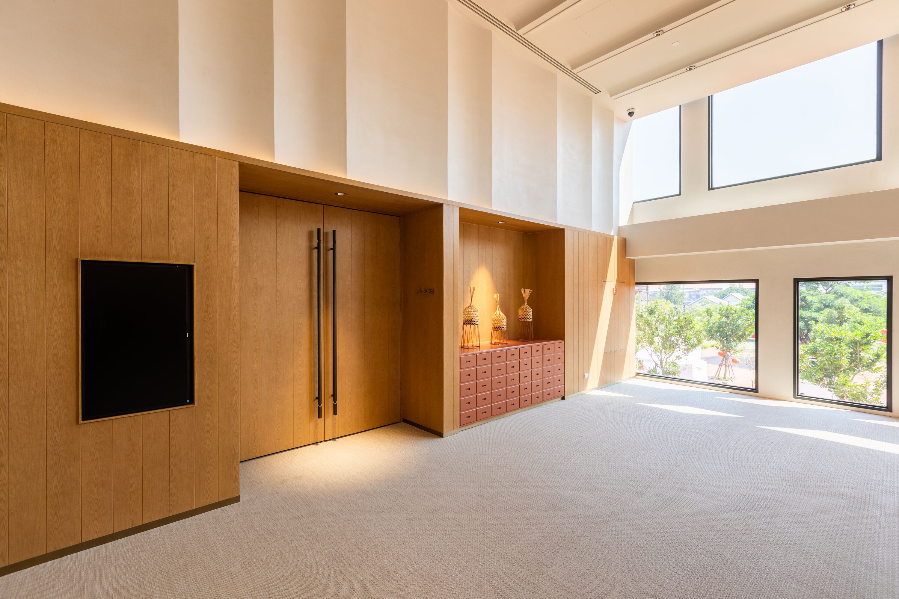 Una habitación amplia con un gran ventanal, un televisor de pantalla plana montado sobre un panel de madera y un mueble de almacenamiento rosa.