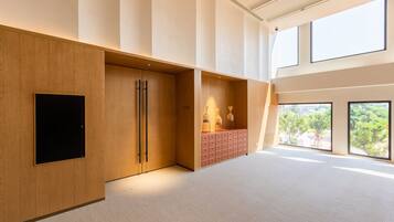 Una habitación amplia con un gran ventanal, un televisor de pantalla plana montado sobre un panel de madera y un mueble de almacenamiento rosa.