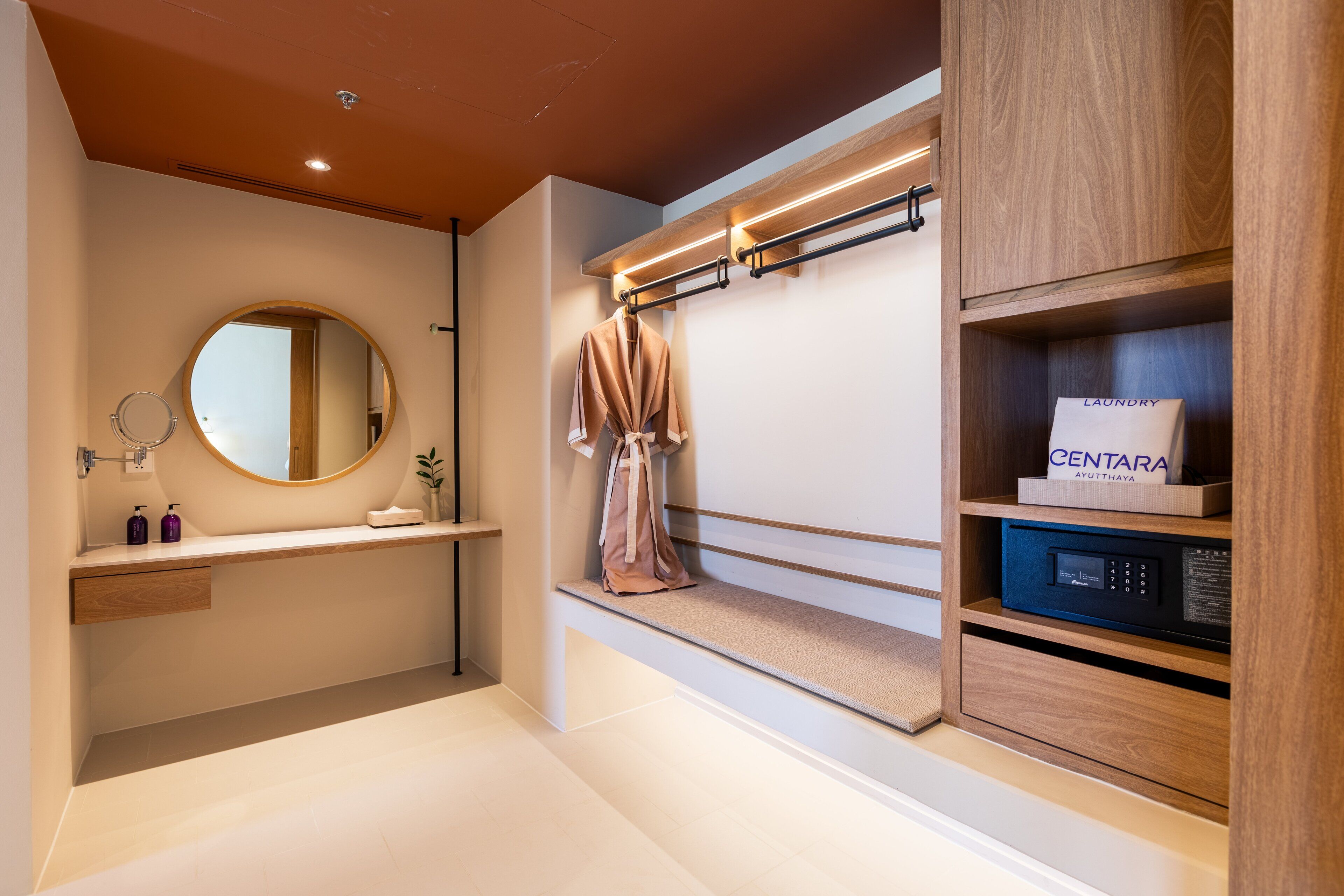 A modern bathroom with a wooden vanity, a round mirror, a towel rack, and a built-in laundry machine.