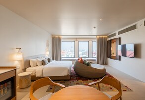 Una habitación de hotel moderna con una cama grande, un sillón de peluche, una mesa de comedor y un televisor.