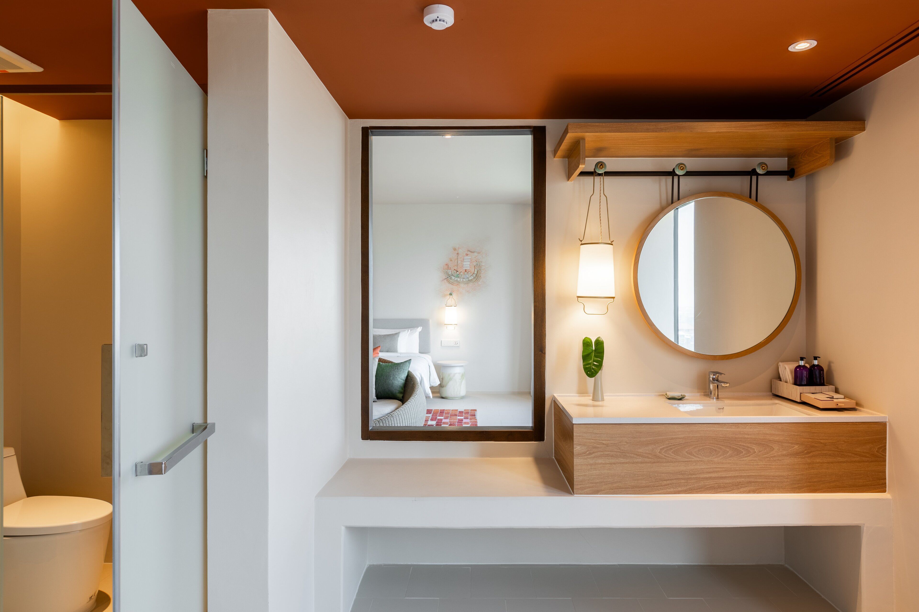 Un bany modern amb un vàter, un lavabo amb un penjador de fusta, un mirall gran i un llum penjada a la paret.
