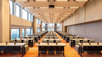 A conference room with rows of tables and chairs, large windows, and a projector on the ceiling.