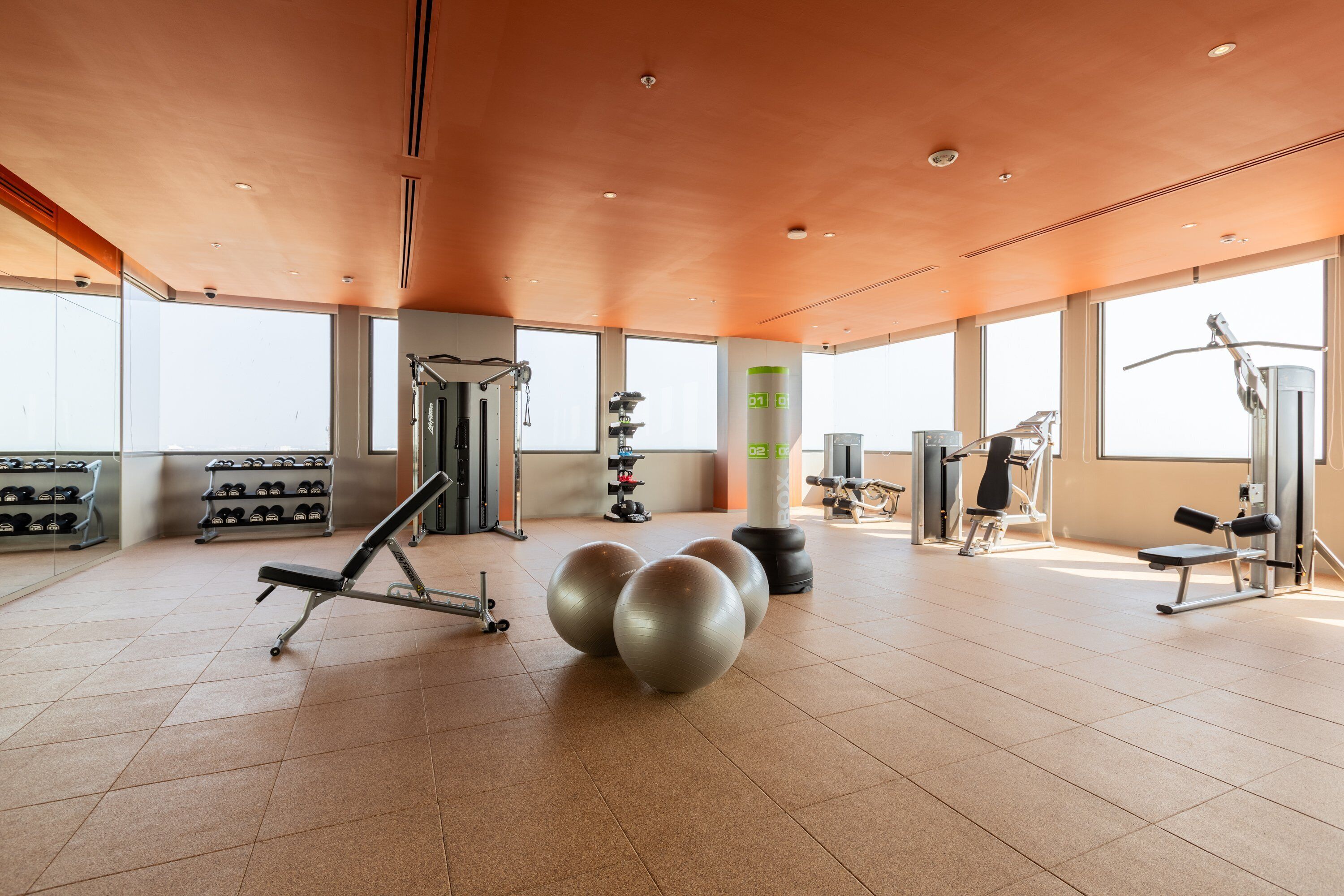 Un gimnasio amplio con diverso equipo de ejercicio, ventanas grandes y un techo alto.