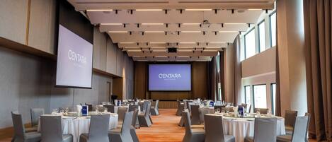 Un salón de conferencias con mesas dispuestas para una reunión, una pantalla grande mostrando 'CENTARA AVUTHTHAIYA' y un diseño de techo moderno.