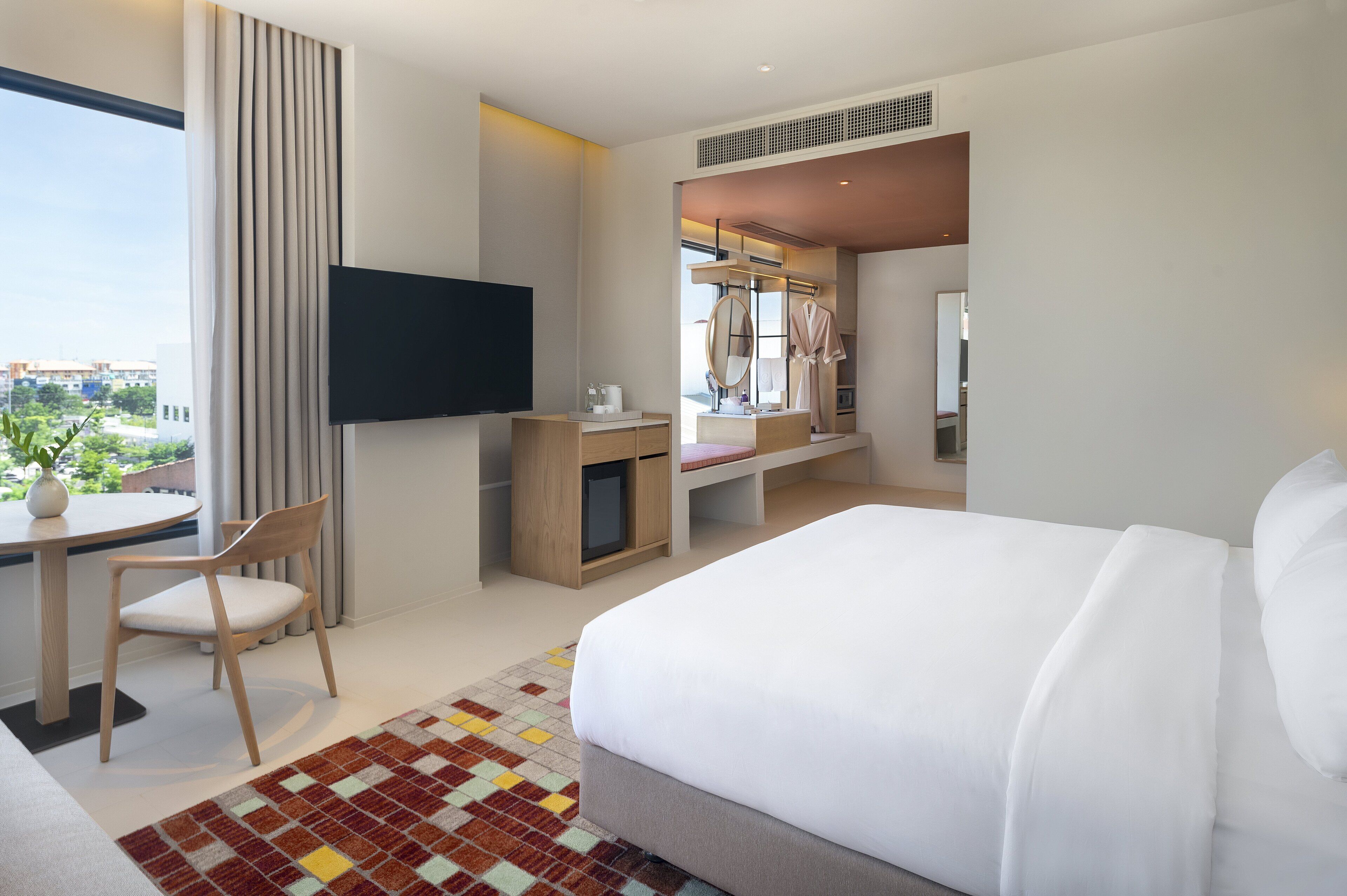 Habitación de hotel moderna con cama, escritorio, silla, televisor y ventana grande con vistas a la ciudad.