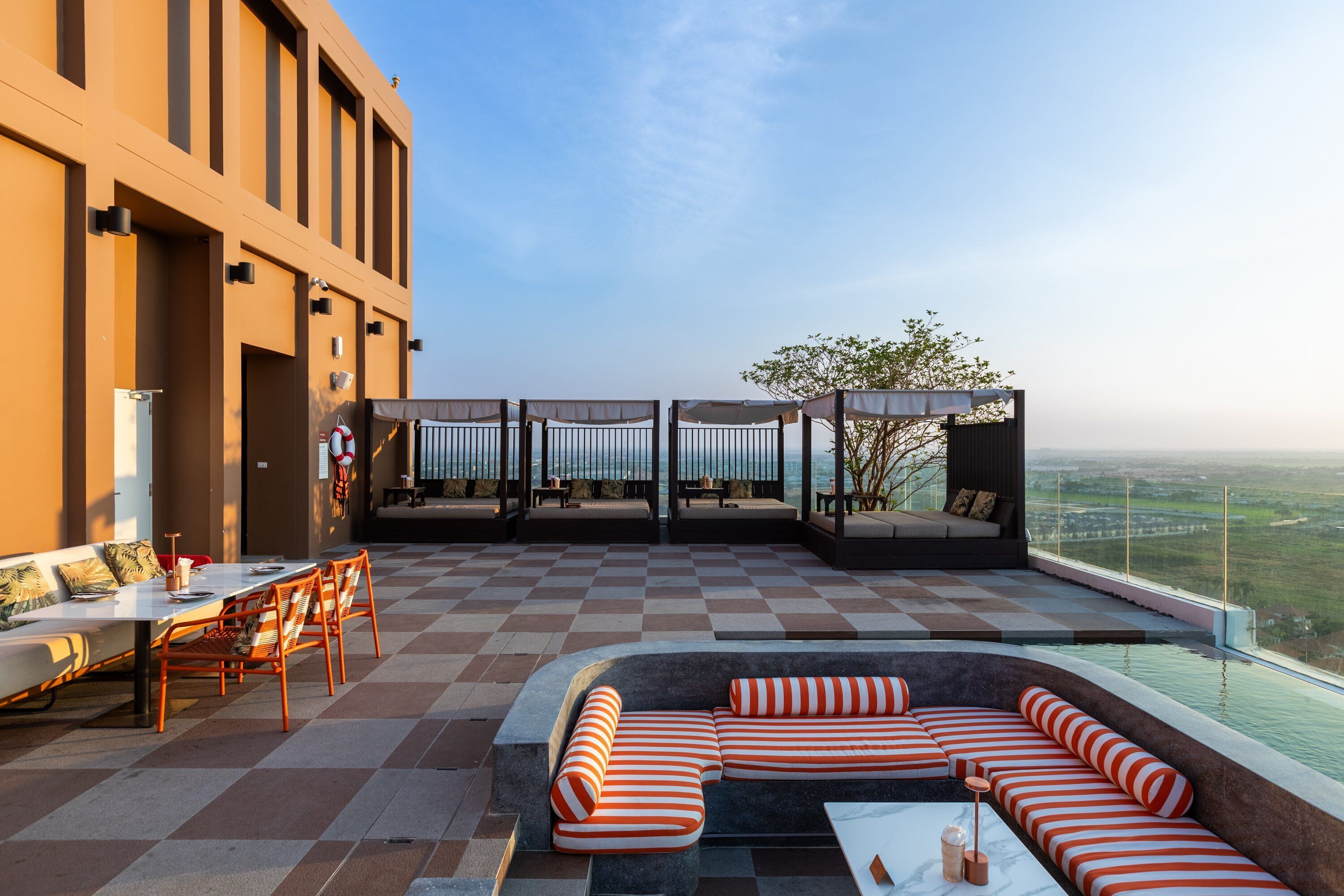 A rooftop terrace with a checkered floor, outdoor seating, and a view of the landscape.