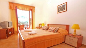 Una habitación de hotel con una cama, un televisor sobre un mueble bajo, dos lámparas de noche, una mesita de noche de madera y un cuadro enmarcado en la pared.
