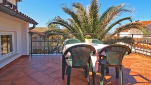 Una terraza con mesa y sillas, rodeada por una barandilla y palmeras.