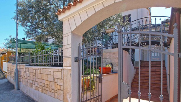 Una entrada protegida por un muro de ladrillo, una reja metálica y una escalera que lleva a un edificio.