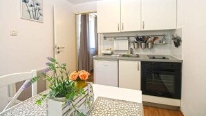 A compact kitchen with white cabinets, a dishwasher, and an oven. There is a dining table with a vase of flowers and a white chair.