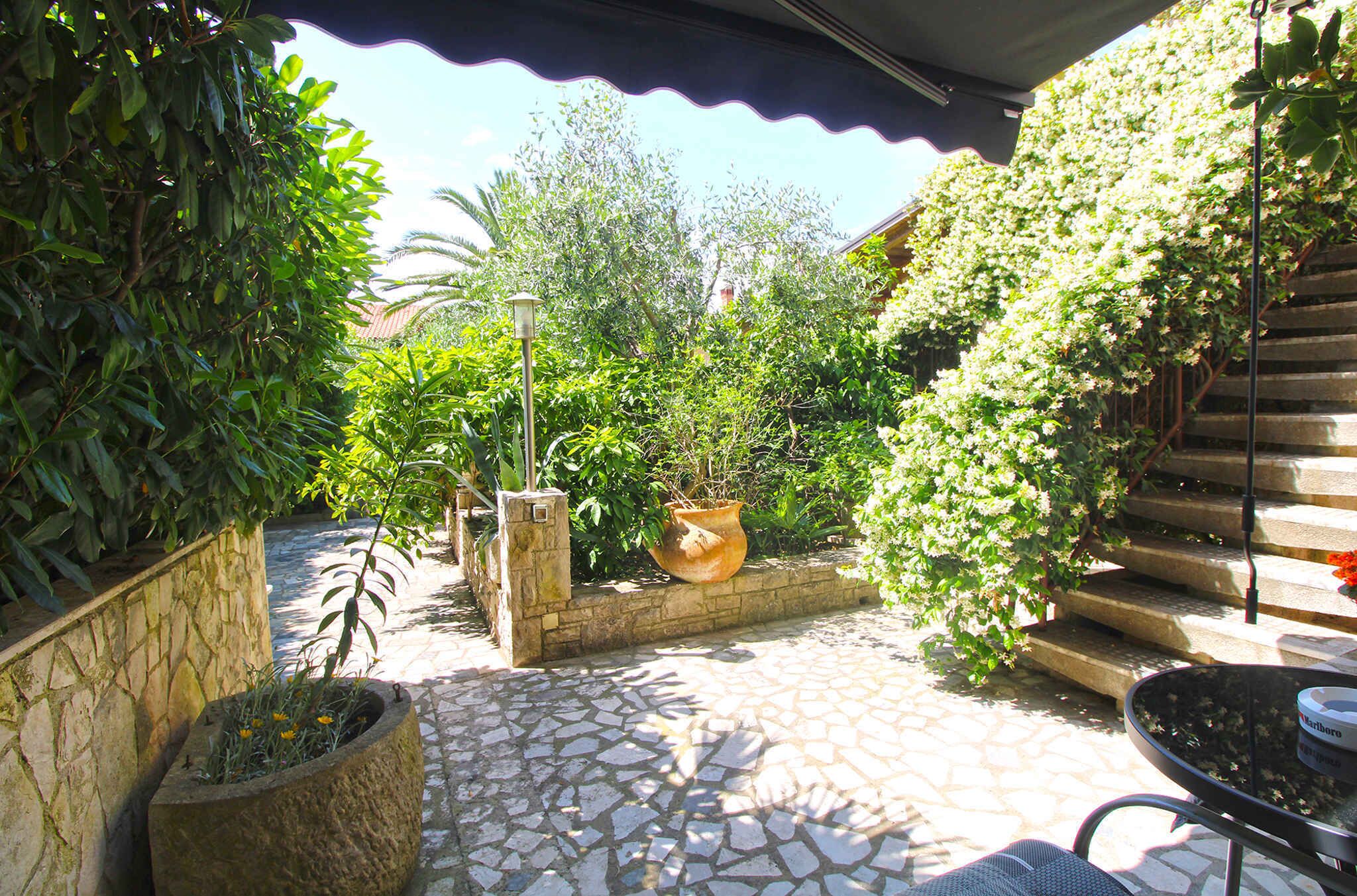 A stone-paved patio with a stone wall, a potted plant, a metal chair, and a staircase with a railing.