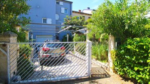 A gated residential area with a parked car, a blue building, and lush greenery.