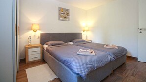 A bedroom with two beds, nightstands, wall-mounted lamps, a rug, and a door.