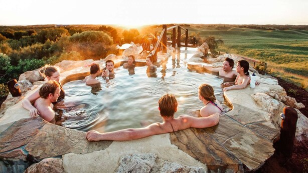 A group of people relaxing in a natural hot spring setting with a wooden bridge and stone structures. - By the Bay - 4pm check out Sundays* (Rosebud)