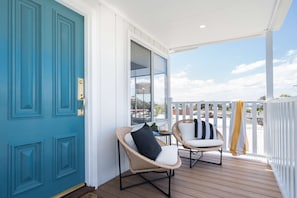 Un porche techado con dos sillas de mimbre, una puerta azul turquesa y vistas del entorno.