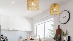 A modern kitchen with white cabinets, a wooden island with bar stools, a coffee machine, and hanging wicker pendant lights. - By the Bay - 4pm check out Sundays* (Rosebud)