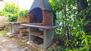 An outdoor stone-built pizza oven with a chimney, surrounded by greenery and a wooden fence. - Holiday apartment with air conditioning (Pula)