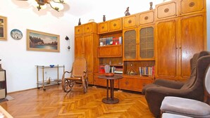 A room with a wooden herringbone floor, a large wooden cabinet with glass doors, a wicker chair, and a small round table. - Holiday apartment with air conditioning (Pula)