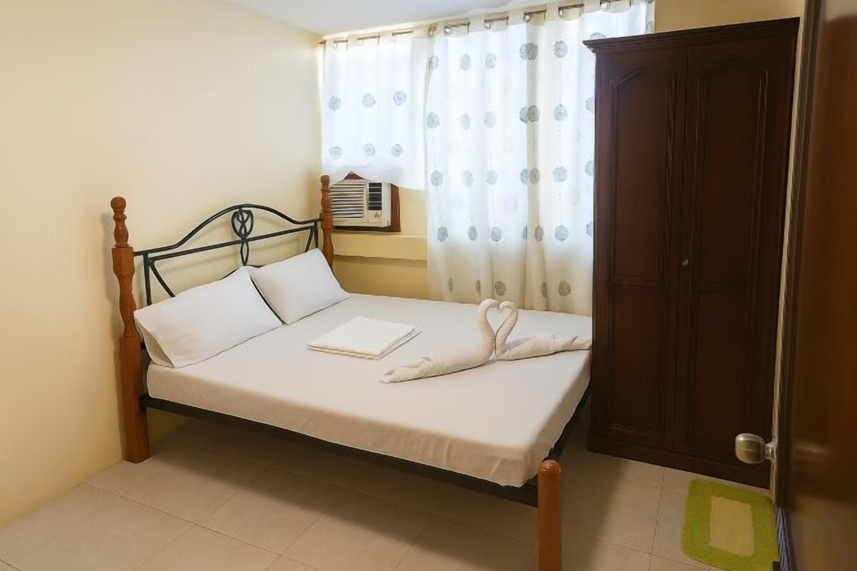 A single bed with a wooden frame, a bedside table, a wall-mounted air conditioner, and a door to a closet.