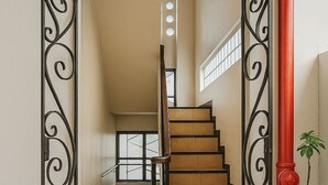 A staircase with a wooden finish, flanked by ornate black metal railings, leading to a landing with a window. - Goland Pension House and Dormitory by SMS Hospitality (Cebu City)