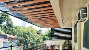 A covered balcony with tiled flooring, a wooden bench, a table with chairs, and potted plants. - Goland Pension House and Dormitory by SMS Hospitality (Cebu City)