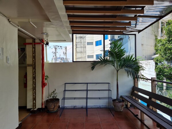 Una habitación con suelo de baldosas, una banca de metal, una palmera en maceta y un ventanal con vistas a un edificio.