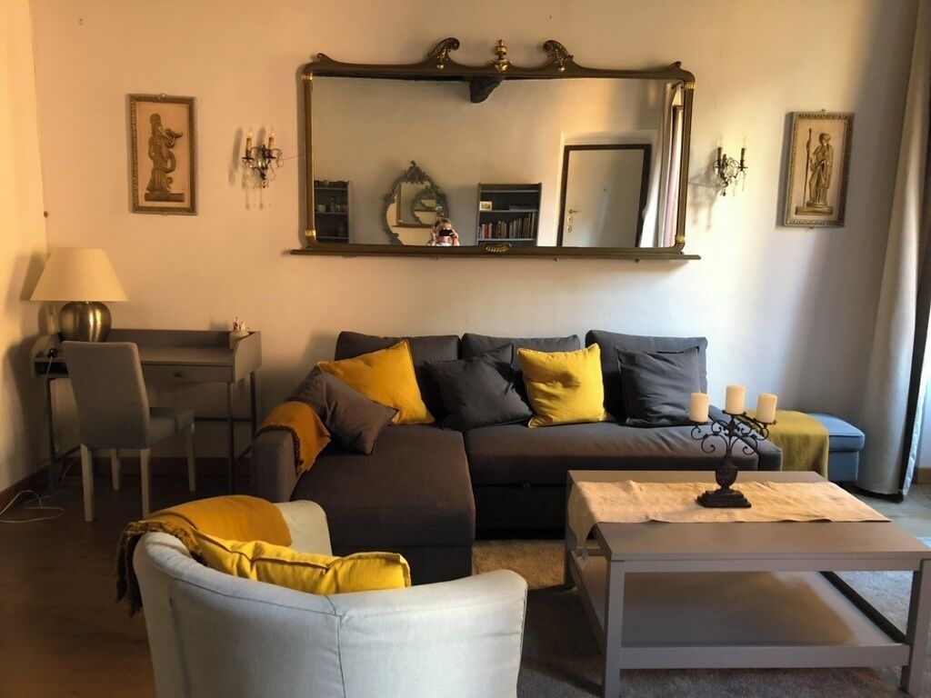 A living room with a dark grey sofa, a white armchair, a small table, and a large mirror on the wall.