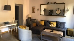 Un salon comprenant un canapé, une table basse, une table à manger avec des chaises, une lampe et un miroir au mur.