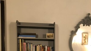 Une bibliothèque grise remplie de livres, un miroir et une petite table sur laquelle se trouve une bougie.