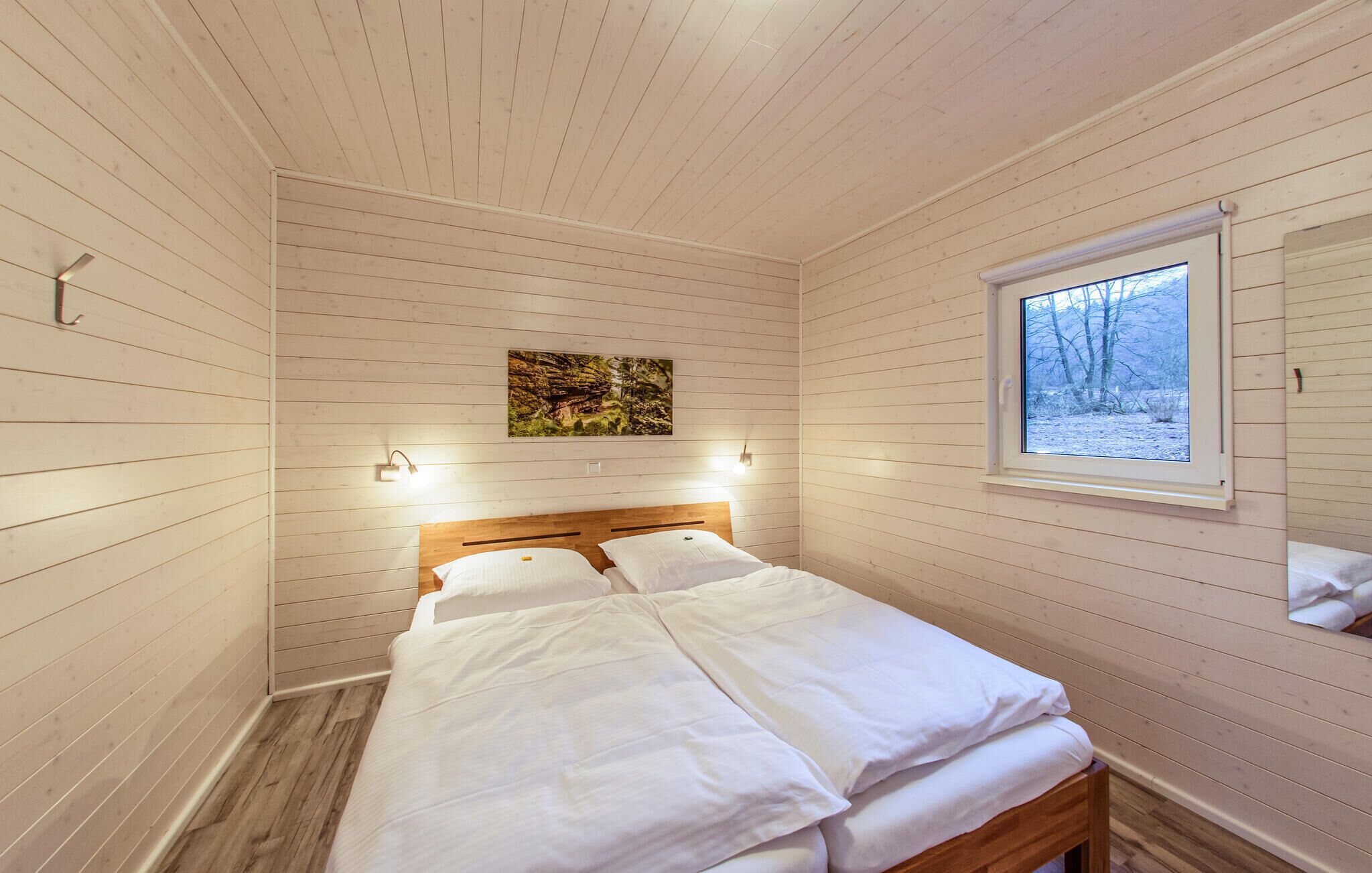 A bedroom with a wooden bed, a window with a view of trees, and a painting on the wall.