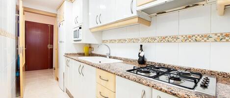 A modern kitchen with white cabinets, a granite countertop, a gas stove, and a microwave.
