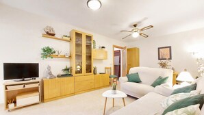 A living room with a TV, wooden cabinet, white sofa, and a ceiling fan.
